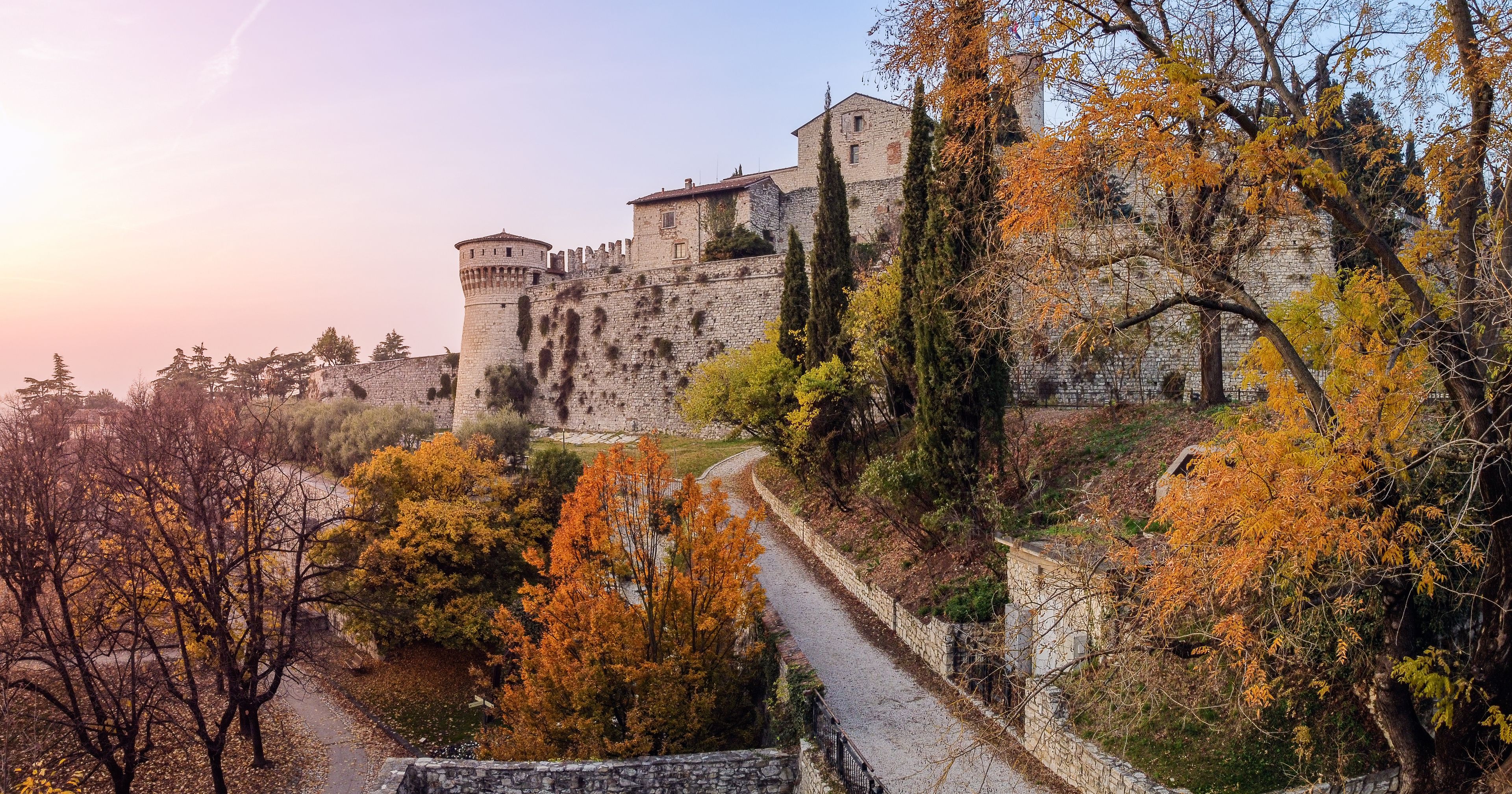 A historic stone castle with a tower, surrounded by autumn-colored trees and a stone pathway.