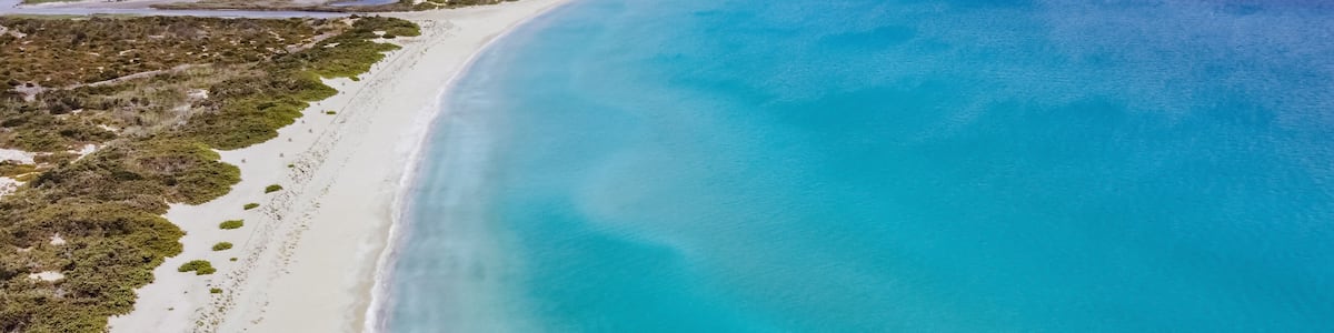 A coastal landscape with a sandy beach, clear turquoise waters, and a distant shoreline.