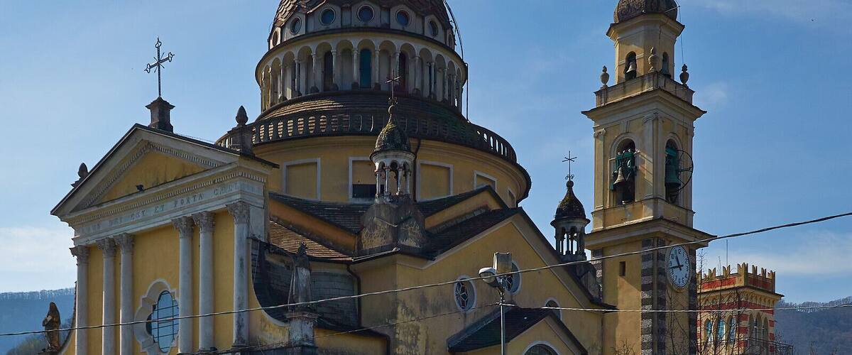 A historic church with a large dome and bell tower, surrounded by parked cars and a clear sky.