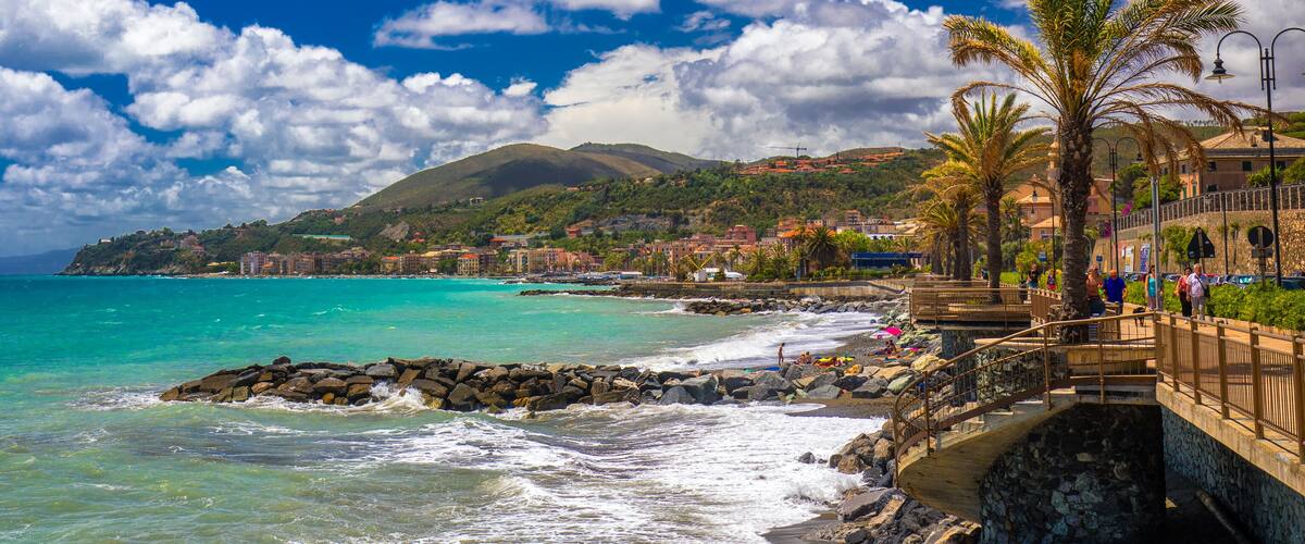 A coastal town with turquoise waters, a rocky breakwater, and a mountain in the background.