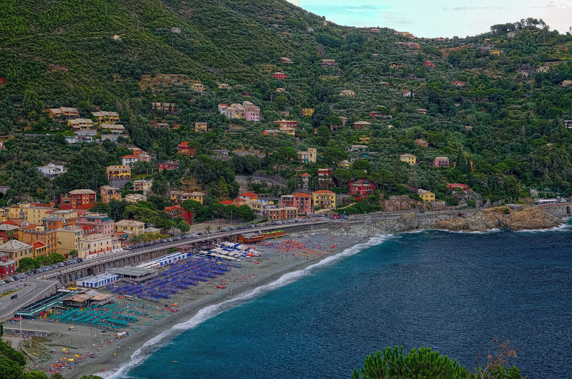 A coastal town with colorful buildings on a hillside, a beach with umbrellas, and the sea.