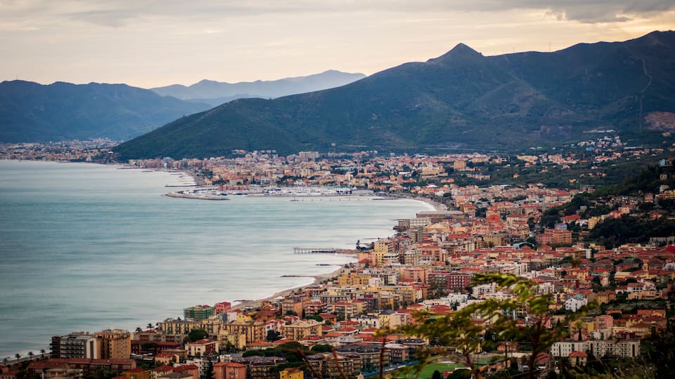 A coastal city with a beach, mountains in the background, and a mix of residential and commercial buildings.