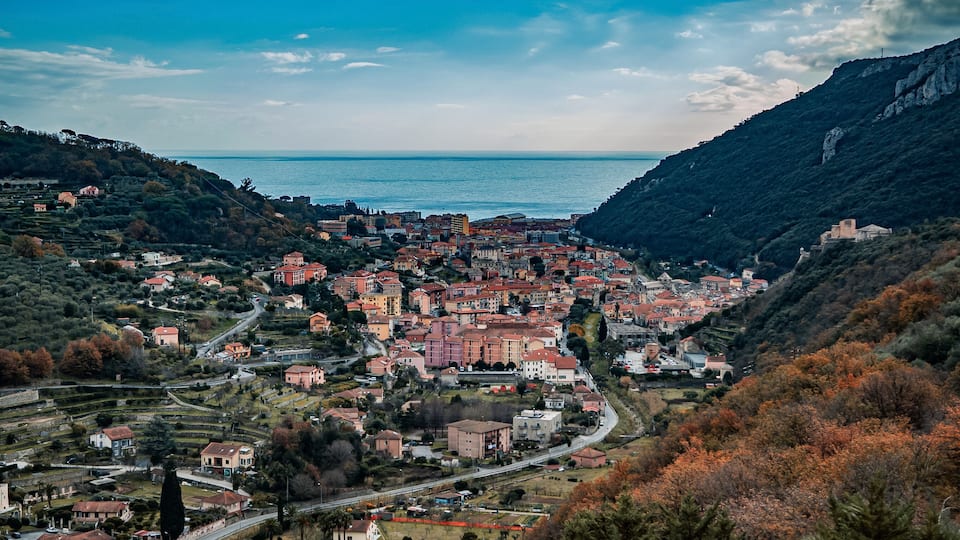 A coastal town with terraced fields, a winding road, and a mountainous backdrop.