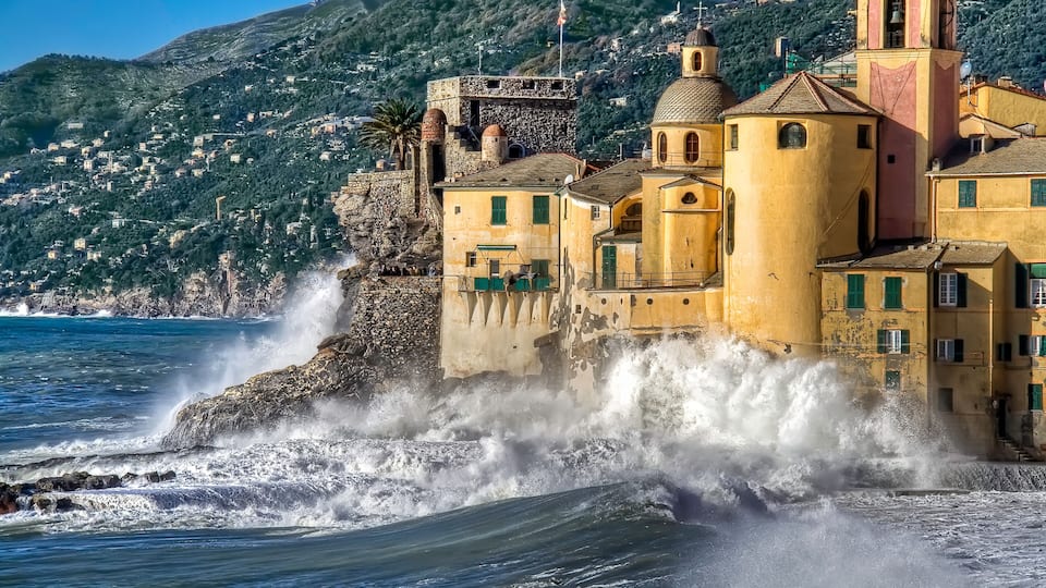 A coastal town with historic buildings, a church, and waves crashing against the shore.