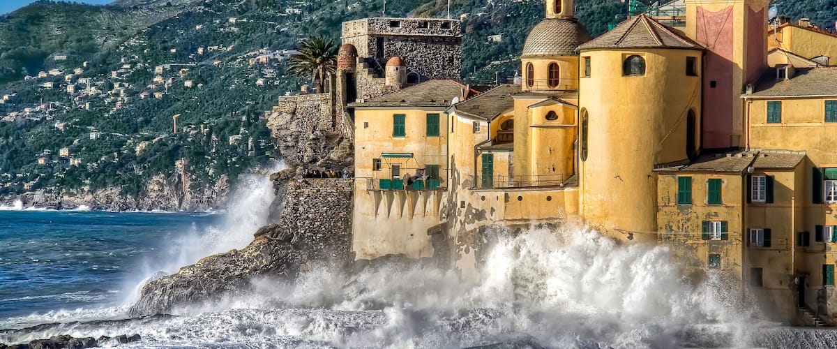 A coastal town with historic buildings, a church, and waves crashing against the shore.