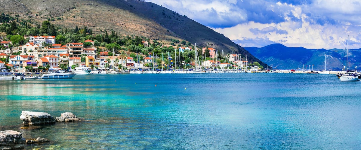 A coastal town with colorful buildings, a marina with boats, and a mountainous backdrop.