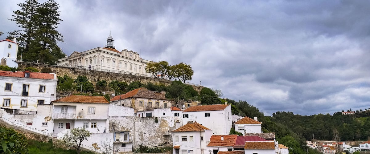 Un bâtiment historique situé sur une colline, avec des maisons aux toits de tuiles rouges en contrebas.