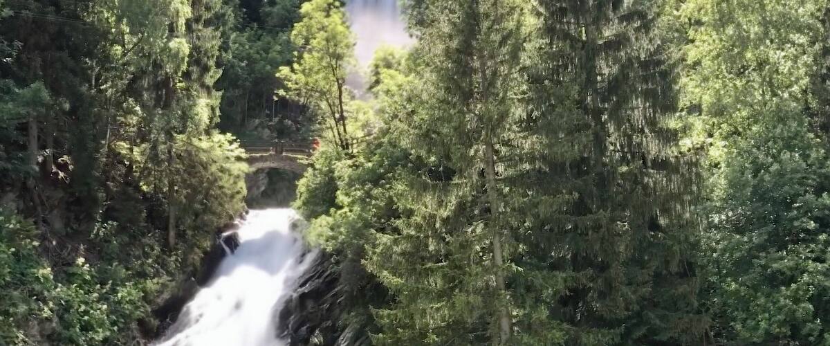 A waterfall cascading through a forested gorge with dense trees and rocky terrain.