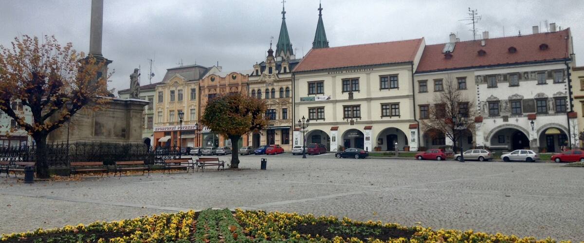 A square with a monument, benches, and flower beds.