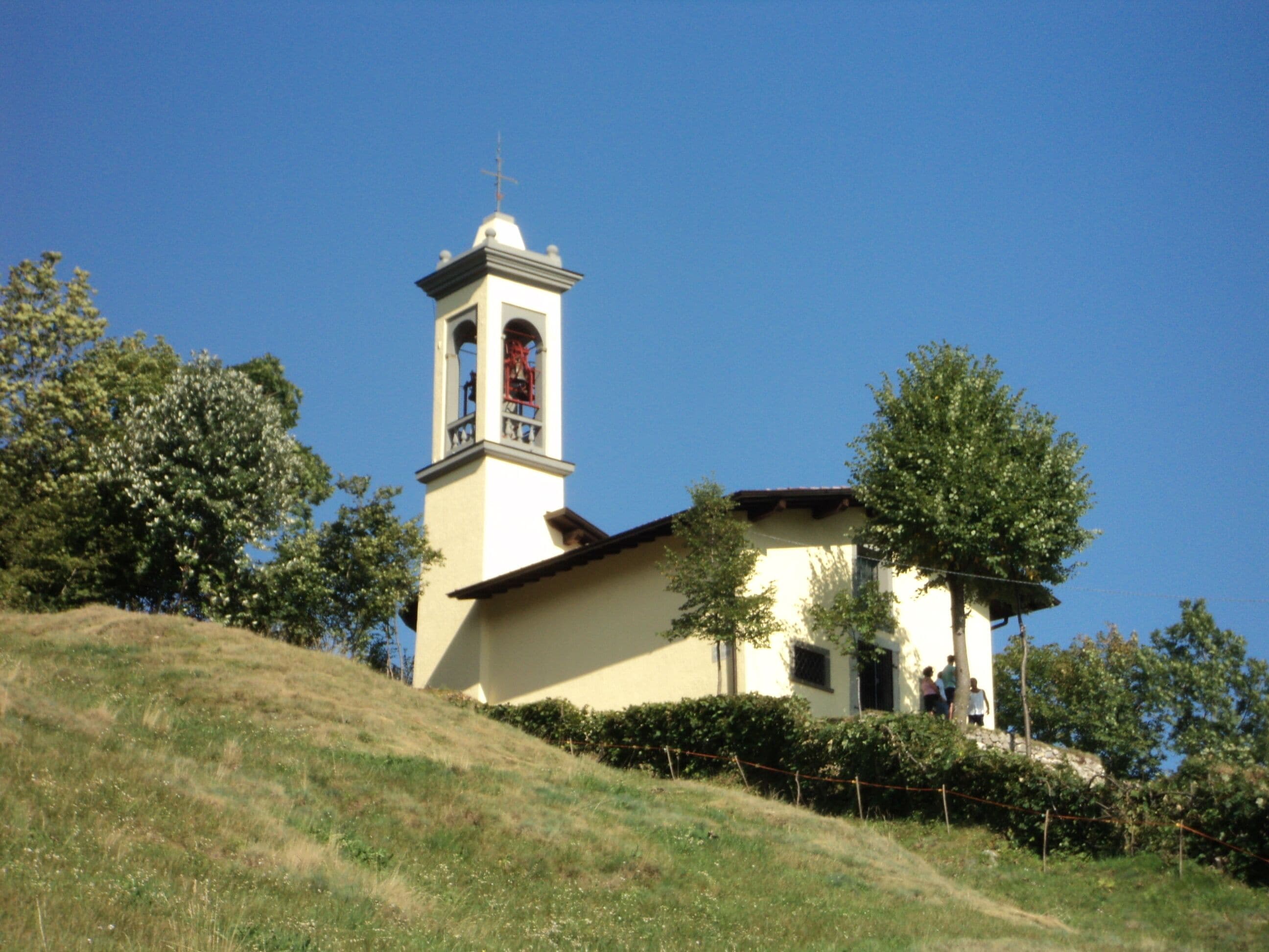 A church with a bell tower on a grassy hill.