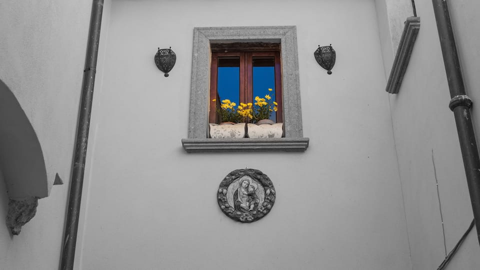 A building facade with a window, decorative wall lights, and a religious plaque.