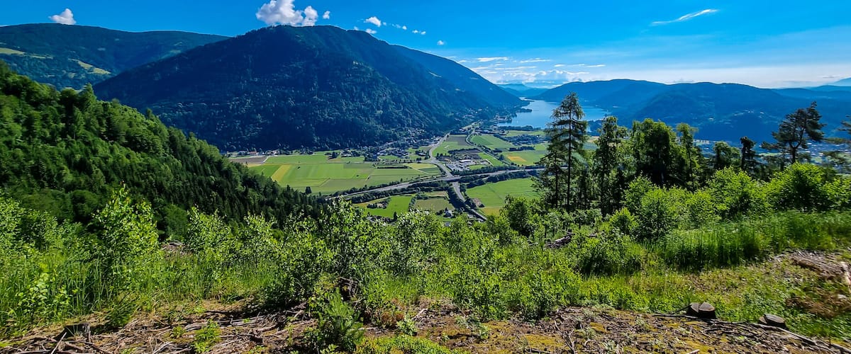 A mountainous landscape with a lake, green fields, and a clear blue sky.