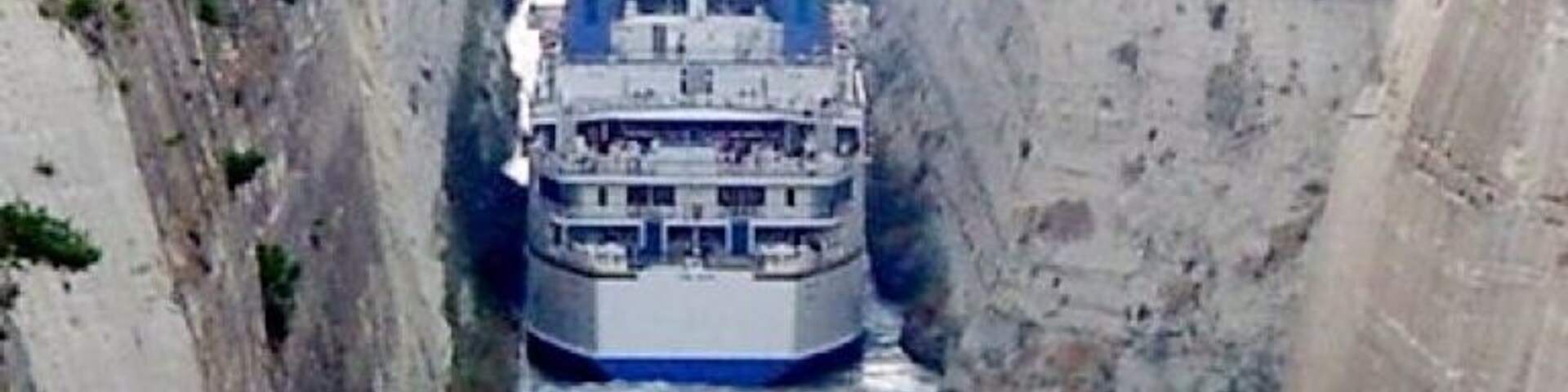 Un barco grande navegando por una estrecha vía fluvial entre altos riscos.