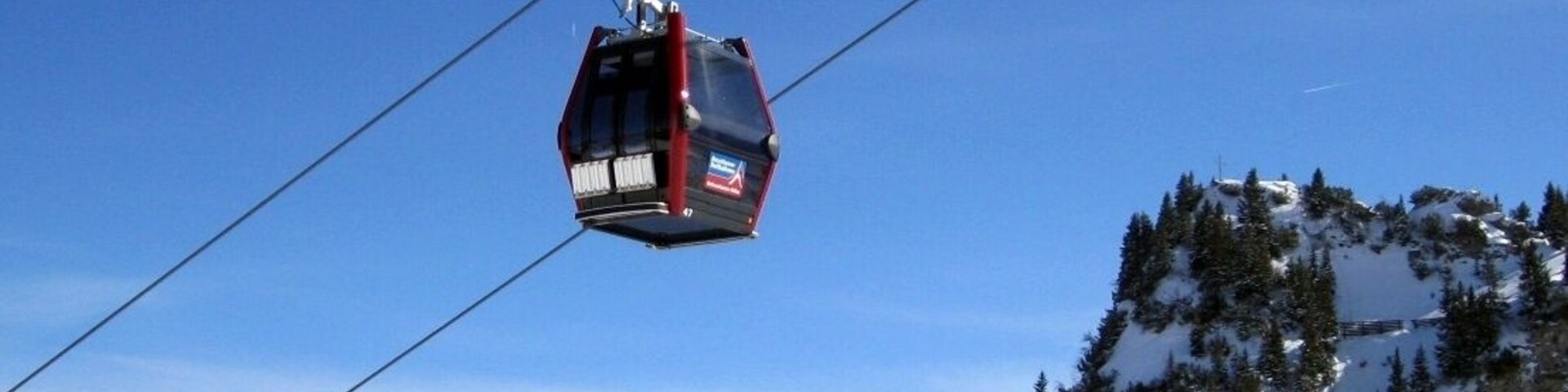Teleférico suspenso sobre uma paisagem montanhosa coberta de neve, com céu claro.