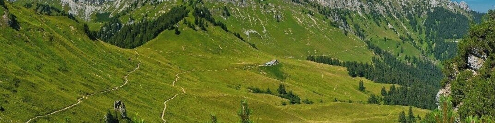 Paisagem montanhosa com trilha sinuosa, florestas densas e picos acidentados.