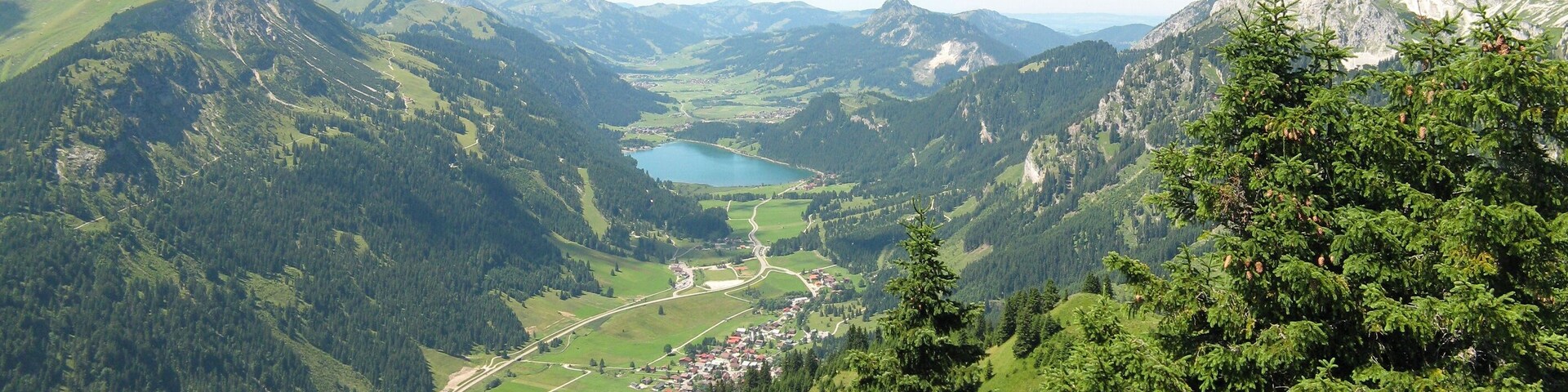 A mountainous landscape with a lake, forested areas, and a small village.