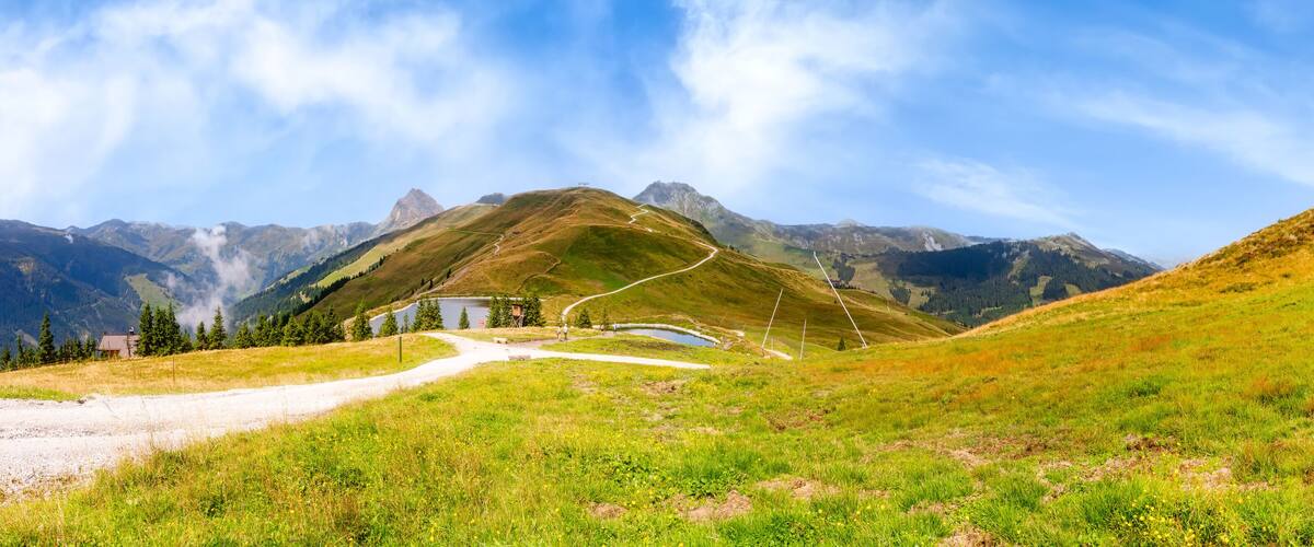A mountain landscape with a winding road, a small building, and a lake.