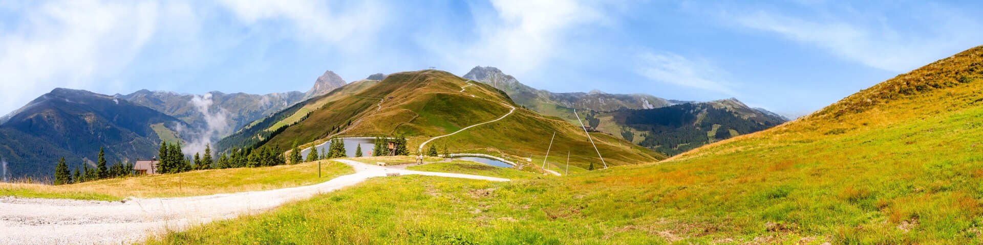 A mountain landscape with a winding road, a small building, and a lake.