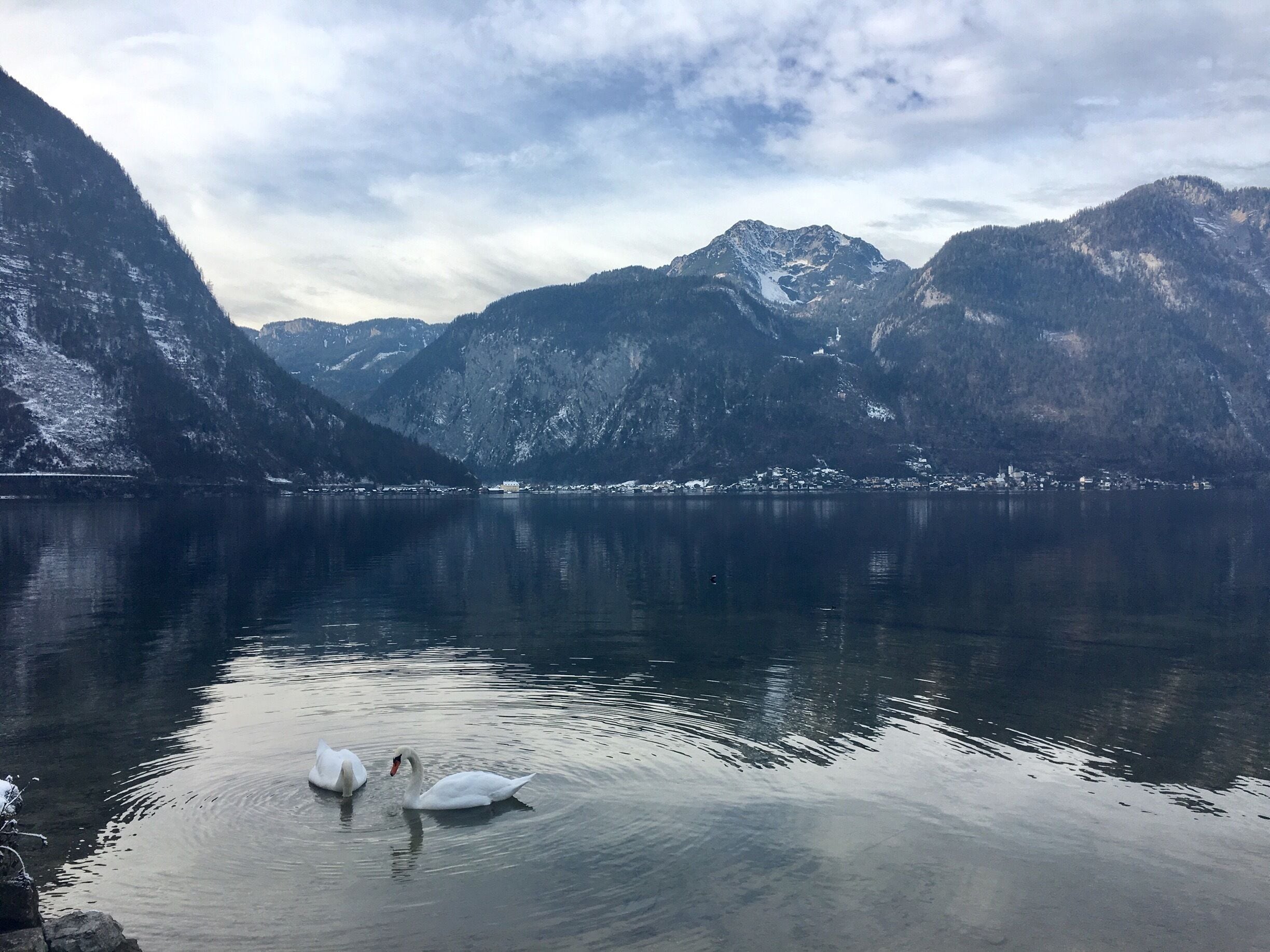A calm lake surrounded by snow-capped mountains and a small town in the distance.