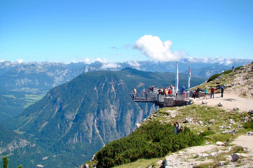 Un mirador con barandilla metálica, una bandera y un paisaje montañoso al fondo.