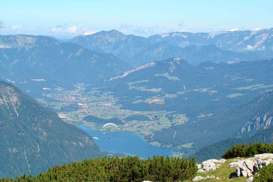 Un paisaje montañoso con un lago, un pueblo y parapentistas.