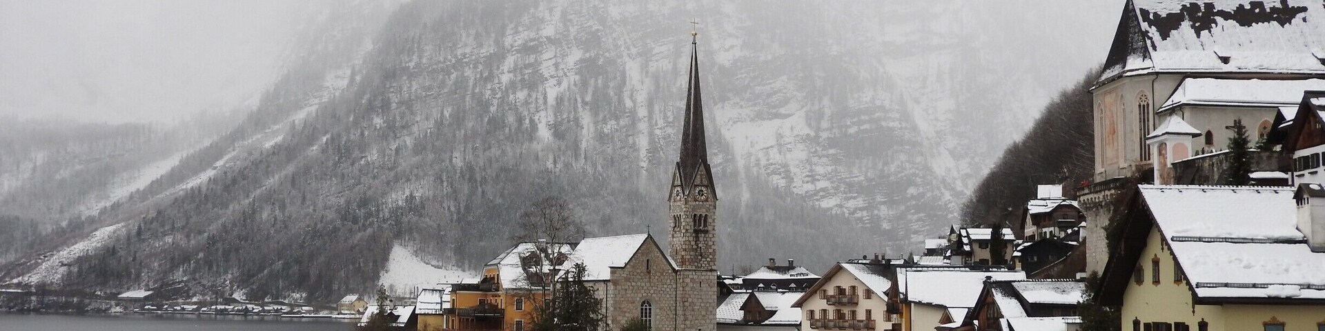 Uma vila coberta de neve, com uma igreja imponente e uma montanha ao fundo.