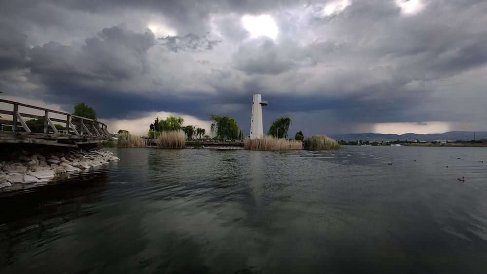 Ein Fluss mit einem weißen Turm, einer Holzbrücke und einem bewölkten Himmel.