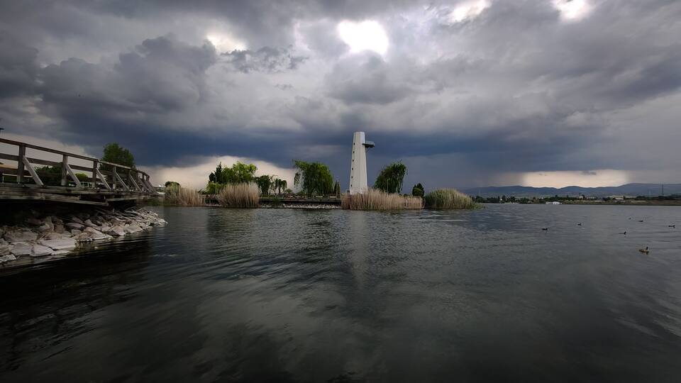 A river with a white tower, a wooden bridge, and a cloudy sky.