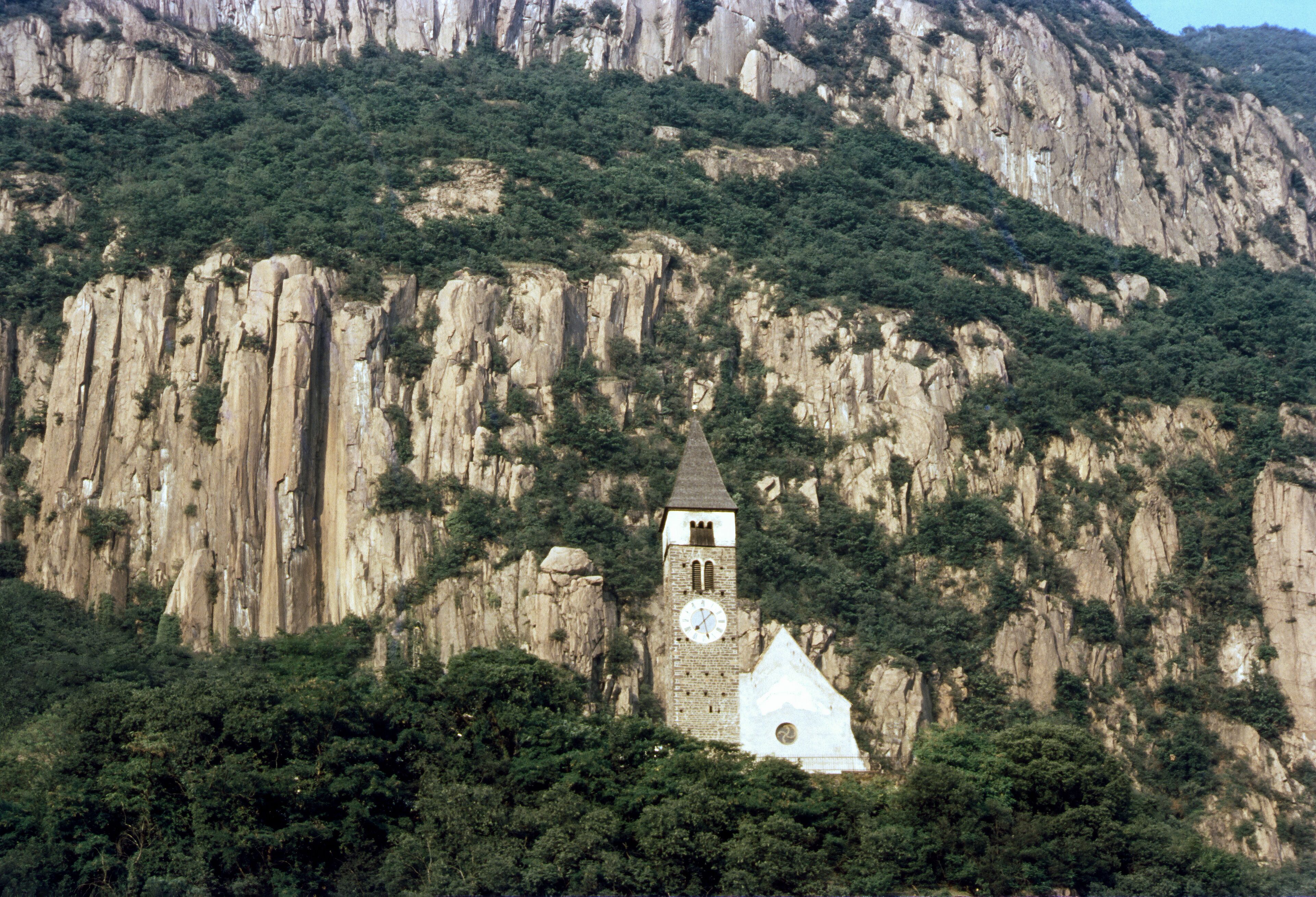 A clock tower on a mountain with steep cliffs and dense greenery.