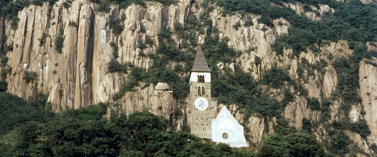 A clock tower on a mountain with steep cliffs and dense greenery.