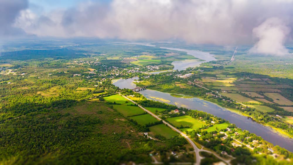 Aerial view over the Landscape of Canada, at Merrickville, Ontario, near the city of Ottawa. A River meanders through the green landscape under blue sky. Drone view, high above the clouds
