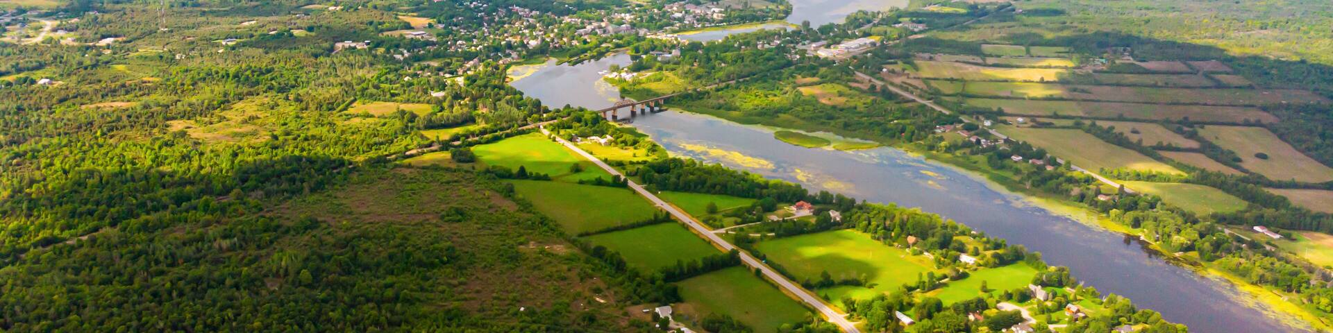 Aerial view over the Landscape of Canada, at Merrickville, Ontario, near the city of Ottawa. A River meanders through the green landscape under blue sky. Drone view, high above the clouds