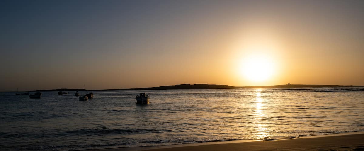 A sunset over a calm sea with several boats anchored.