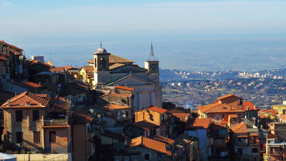 A town with a prominent church featuring a bell tower and dome, surrounded by densely packed buildings with red-tiled roofs.