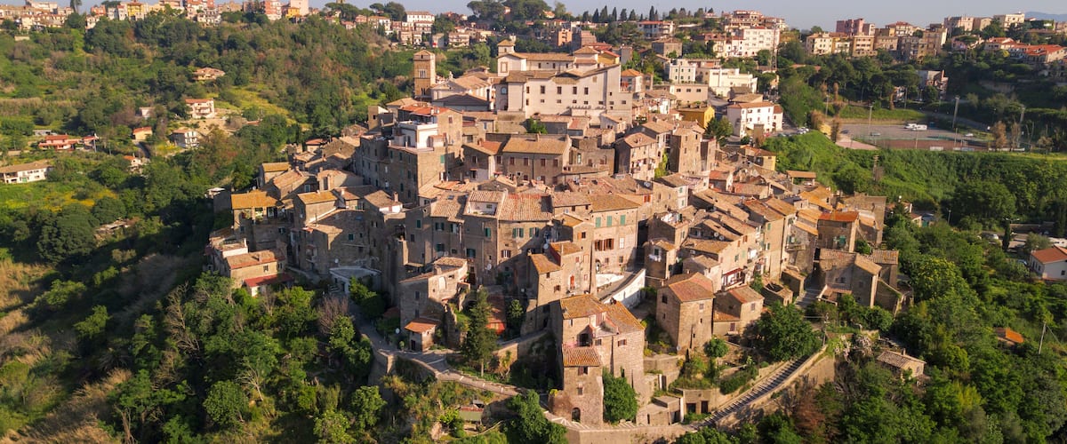 A historic town with medieval architecture, surrounded by lush greenery and hills.