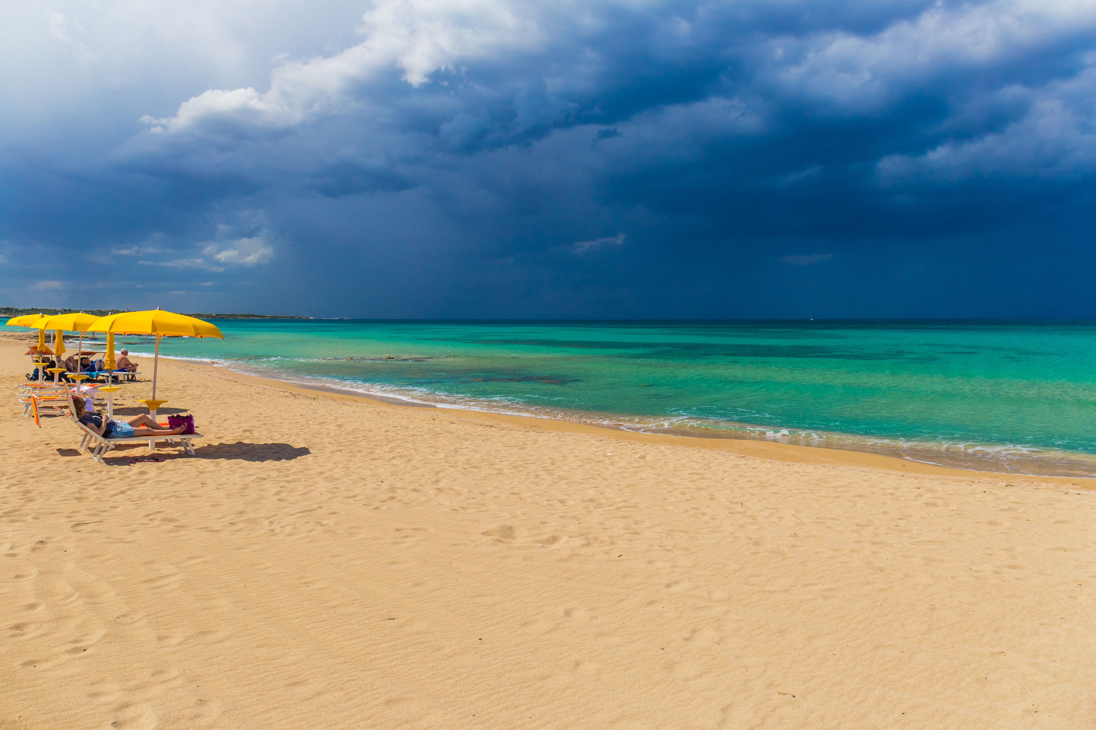 A beach with yellow umbrellas and lounge chairs, a clear sky, and turquoise water.