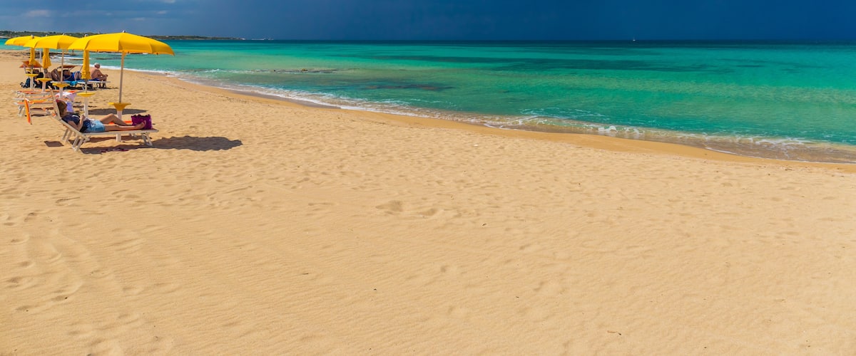 A beach with yellow umbrellas and lounge chairs, a clear sky, and turquoise water.