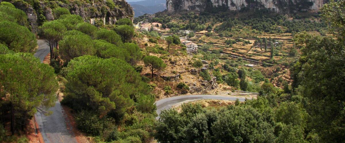 A winding road through a mountainous landscape with dense greenery and rocky cliffs.
