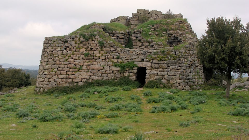 A stone ruin with a central doorway, surrounded by grassy terrain and trees.