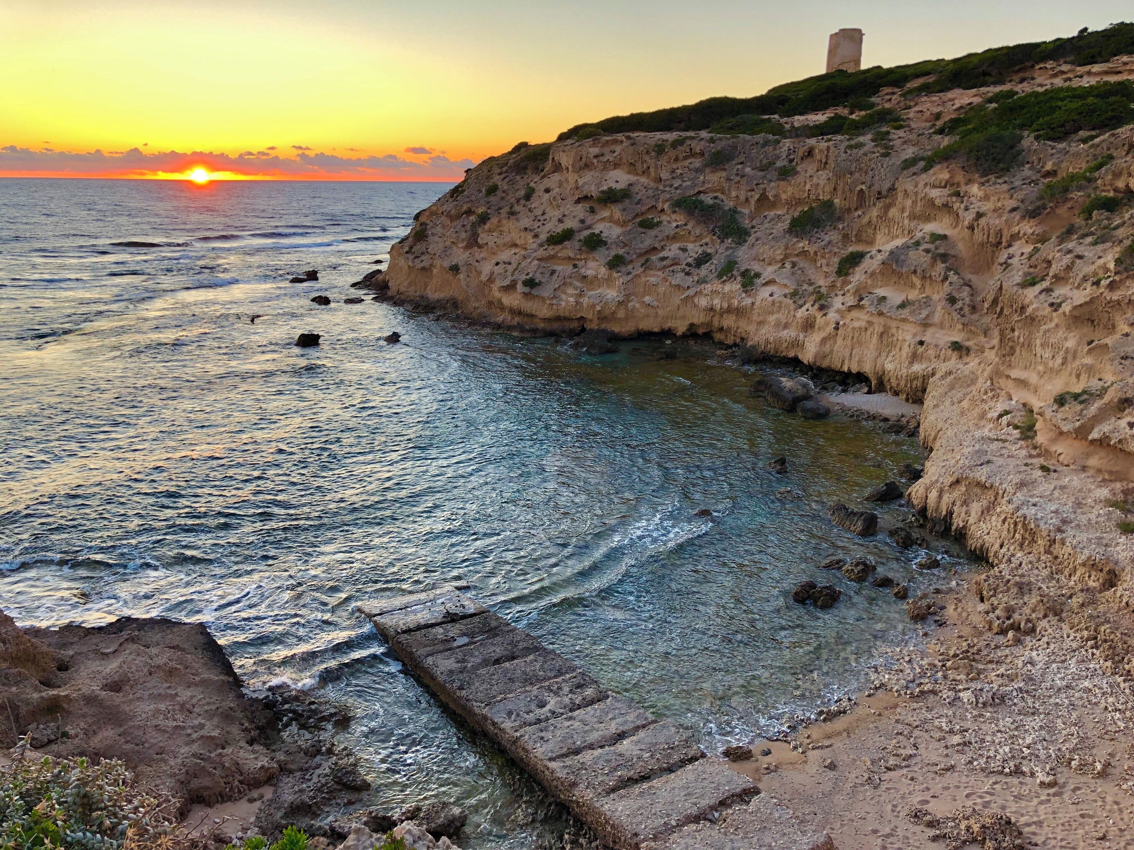 A coastal landscape with cliffs, a clear sea, and a sunset.