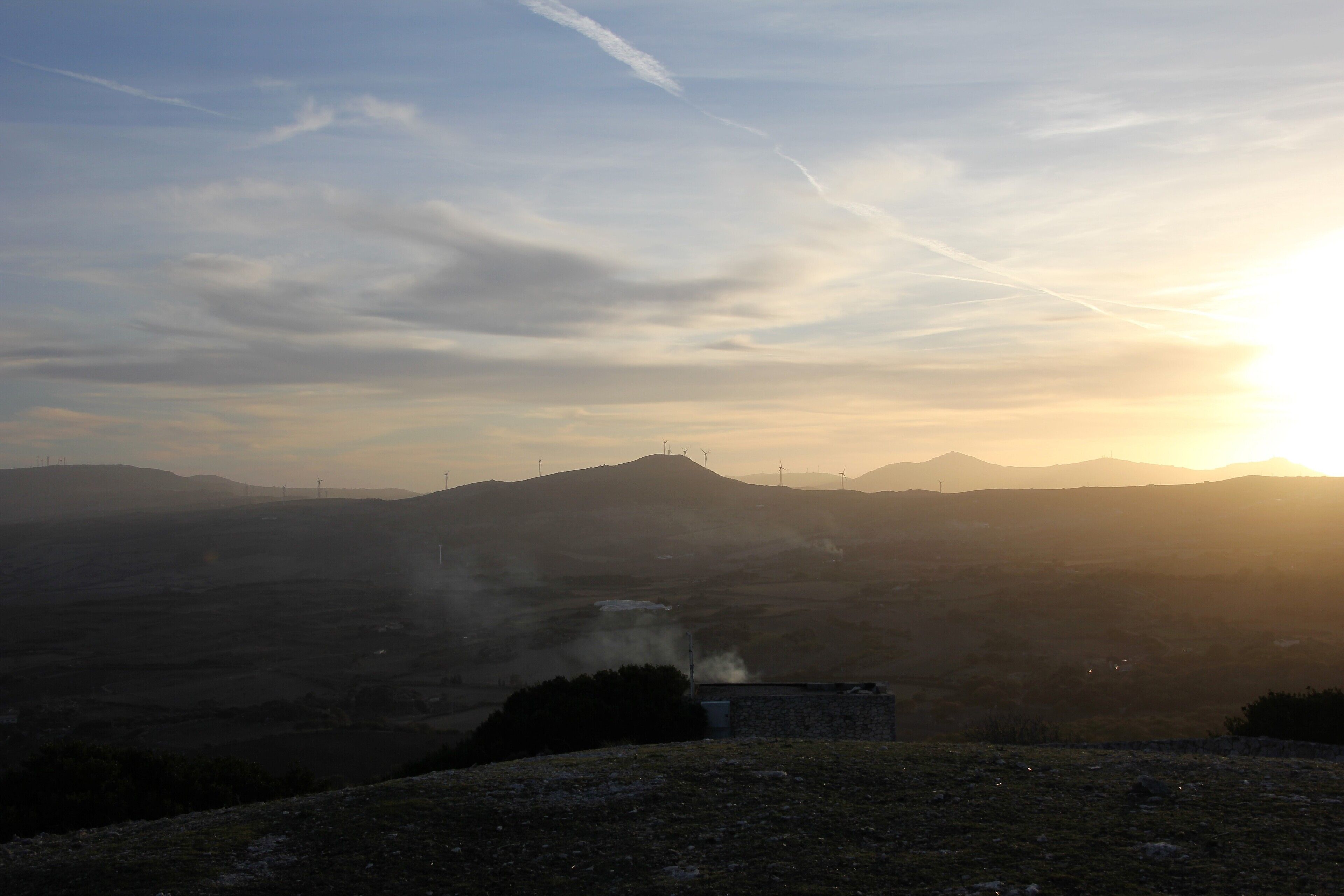 A sunrise over a hilly landscape with a small building emitting steam.