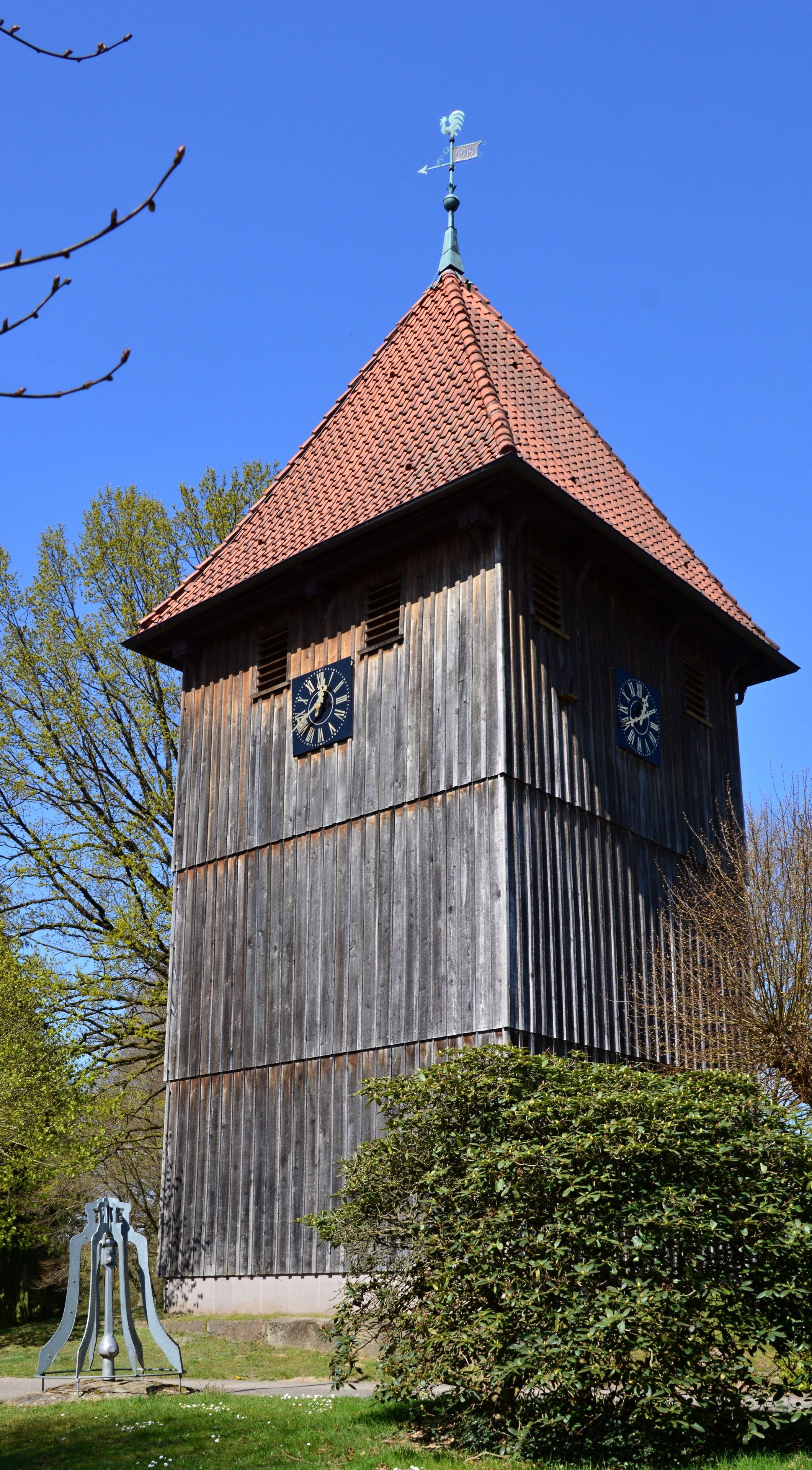 Une tour d’horloge en bois, avec un toit rouge et deux horloges sur ses côtés.