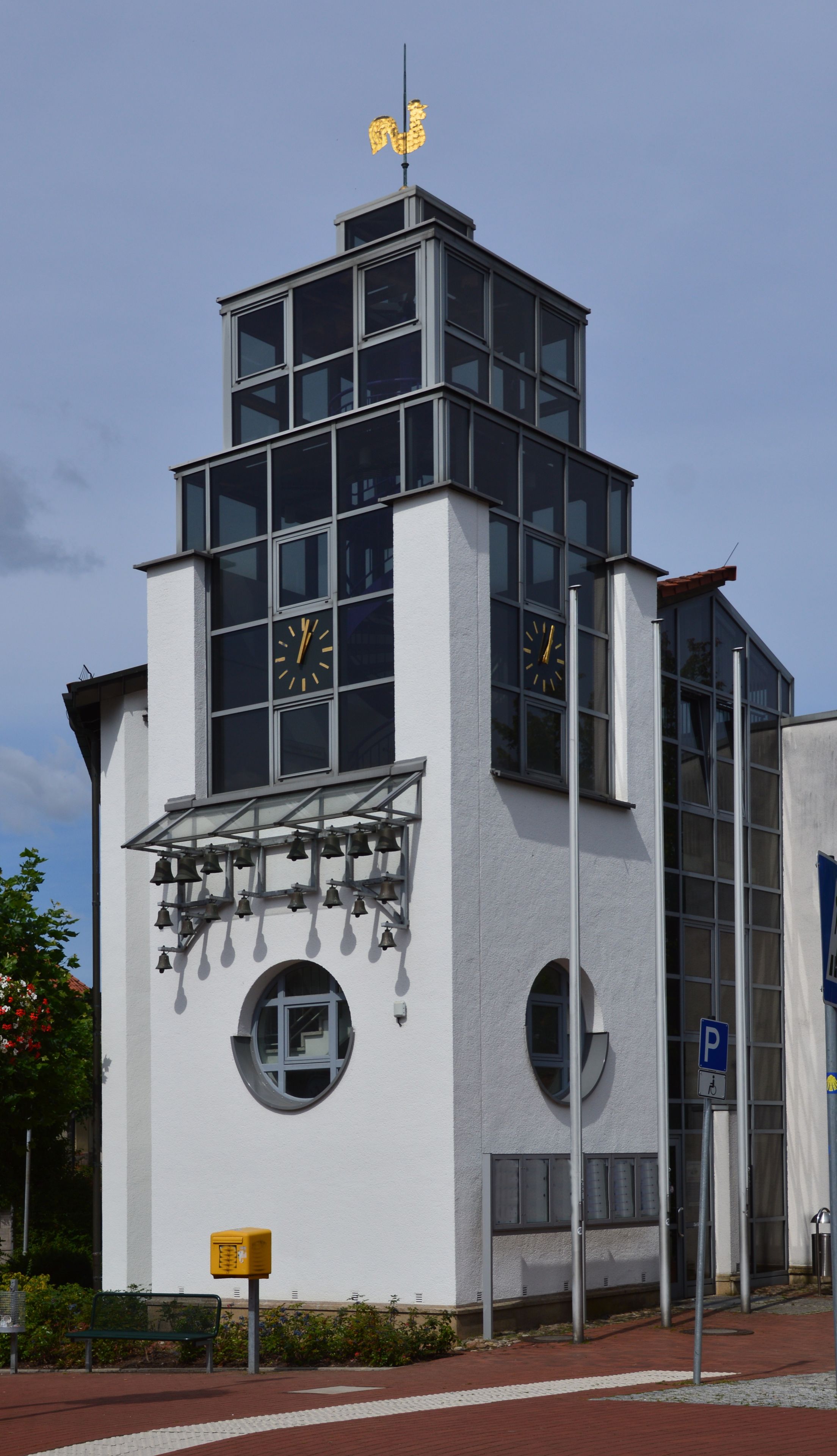 Un bâtiment moderne doté d’une tour horlogée, d’une girouette et d’un panneau indiquant un parking.
