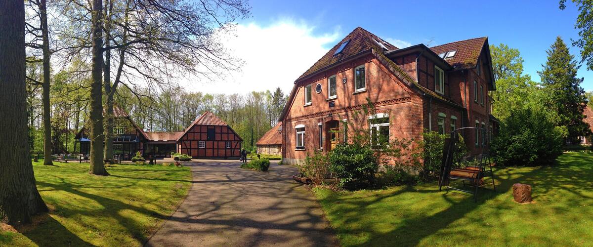 A large brick house with a garden path leading to it, surrounded by trees and greenery.