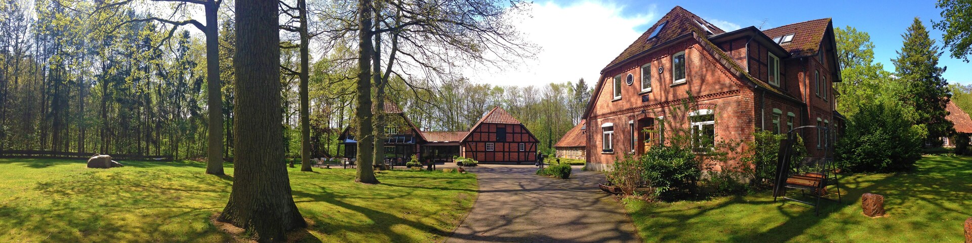 A large brick house with a garden path leading to it, surrounded by trees and greenery.