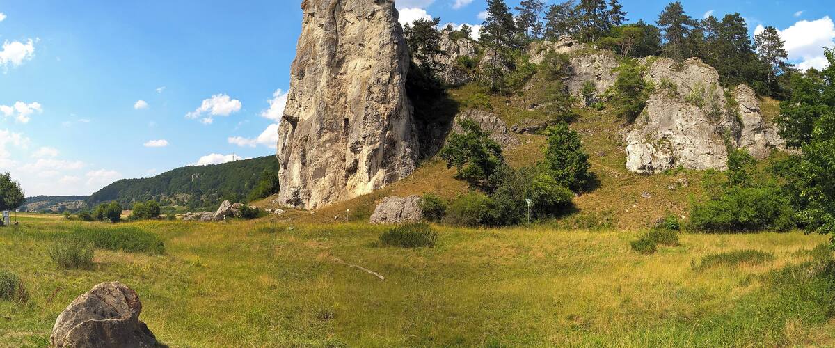 A rocky cliff with a cross at the top, surrounded by greenery and trees.