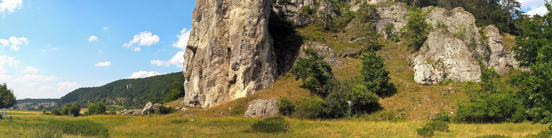 A rocky cliff with a cross at the top, surrounded by greenery and trees.