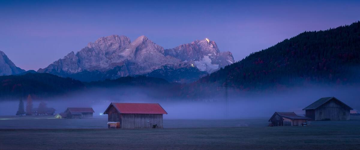 A misty mountain landscape with several wooden buildings and a clear sky.