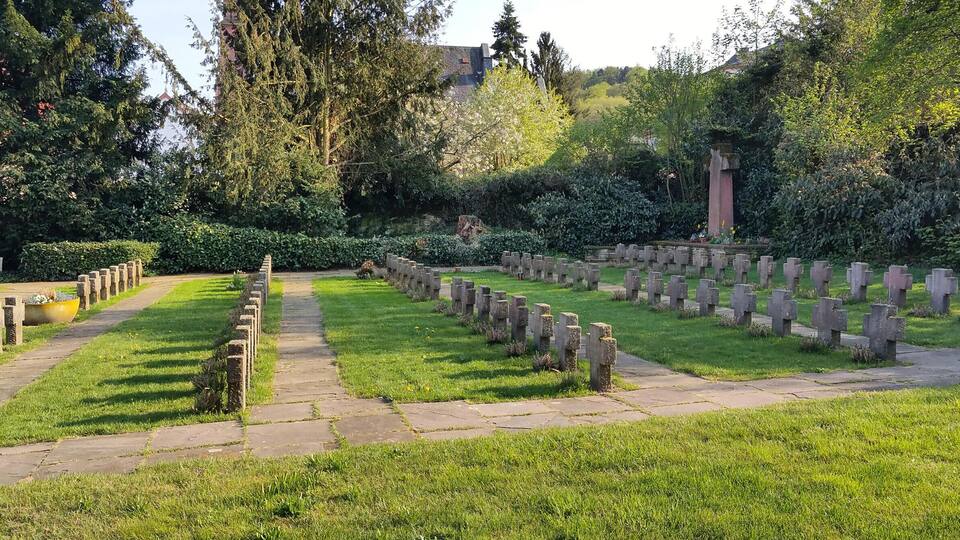 A cemetery with rows of headstones, a stone pathway, and lush greenery.