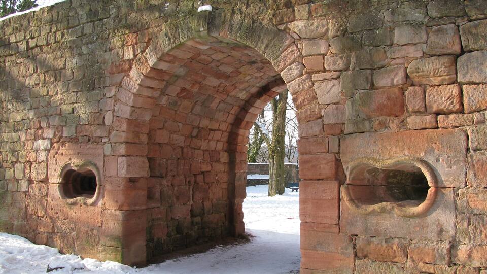 An old stone bridge with arched openings and snow on the ground.